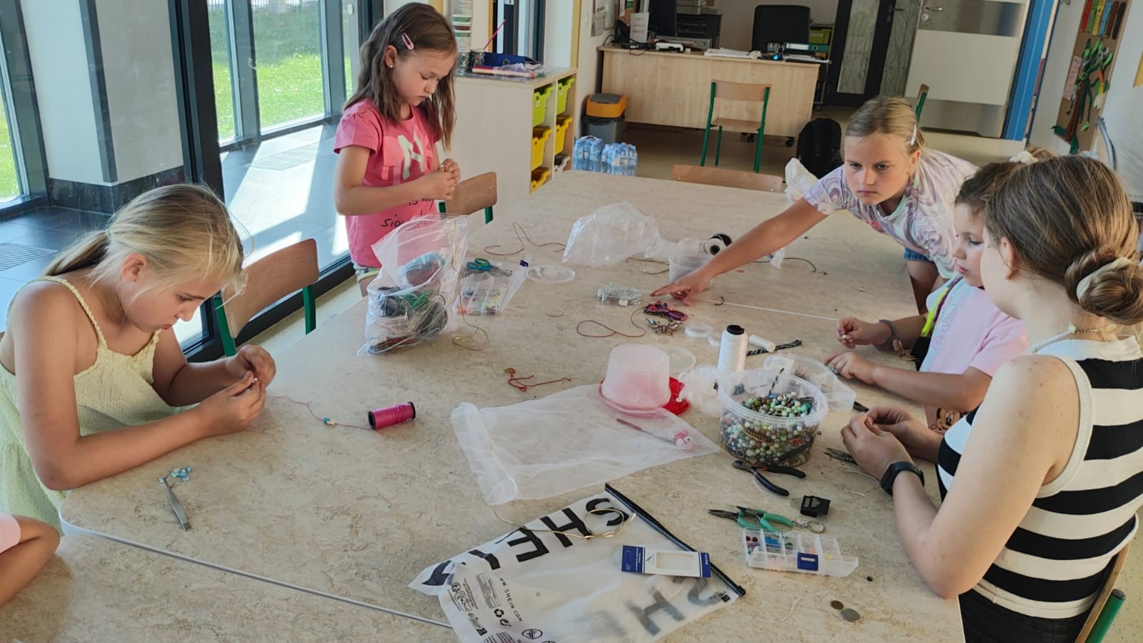 Wokół długiego stołu siedzi grupa dzieci w wieku szkolnym. Na stole leżą kredki i kartki do rysowani