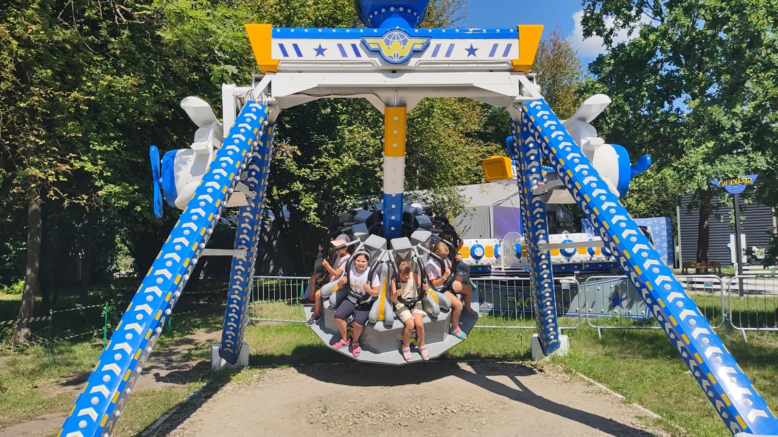 Na dużej wieloosobowej huśtawce siedzi grupa dzieci.